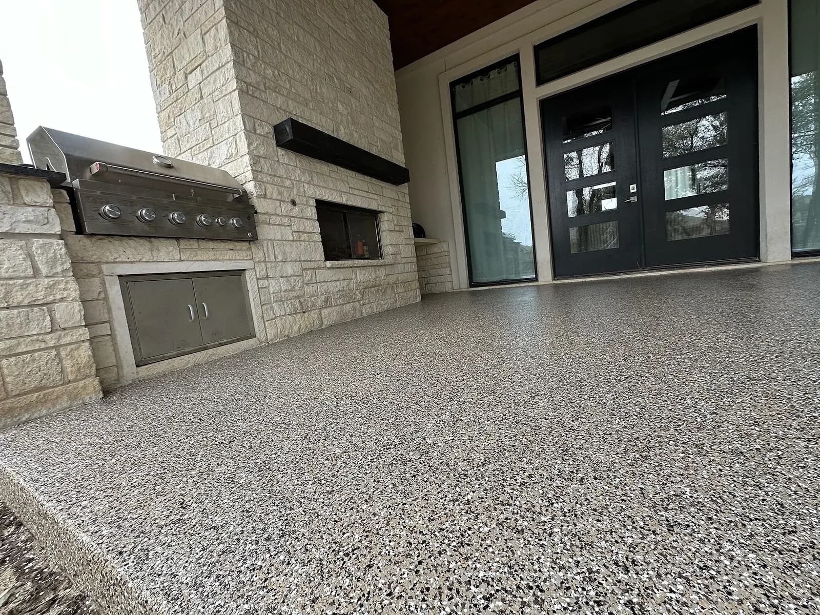 Covered patio with a stone fireplace, grill and coated floor