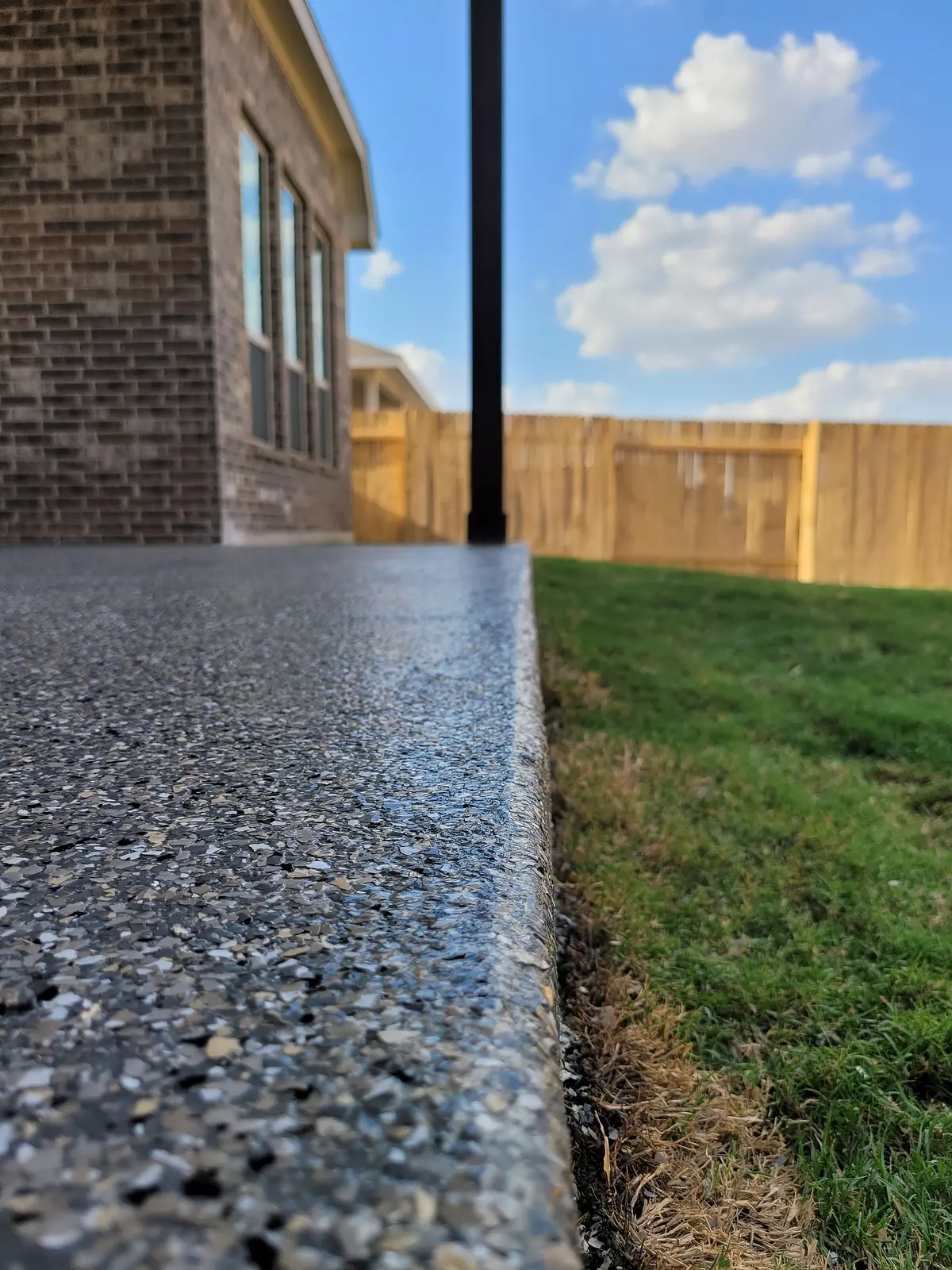 Coated patio edge running beside a fence line and lawn