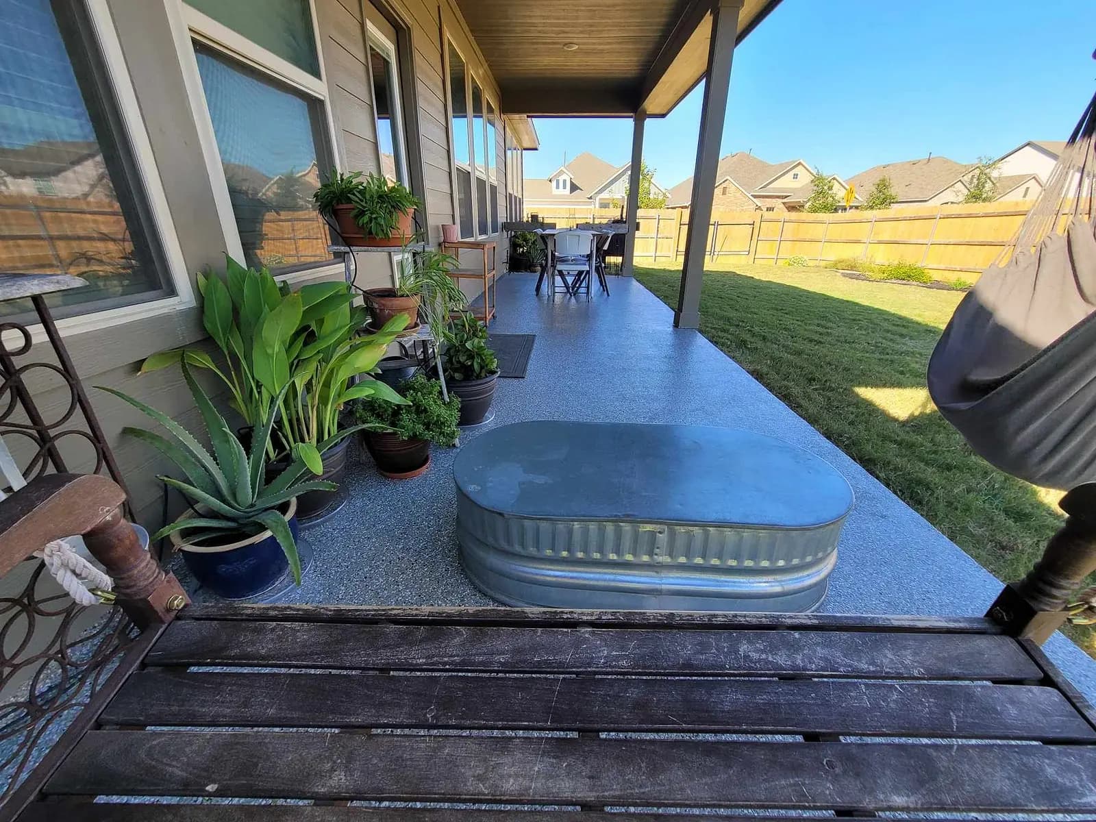 Coated back porch with planters, a stock tank and a bench